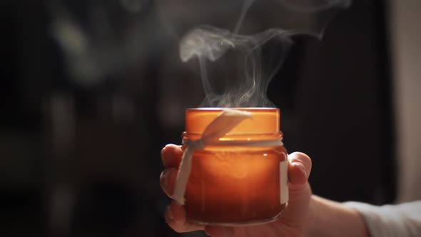 Hand Holding Smoking Aroma Candle in Jar at Home