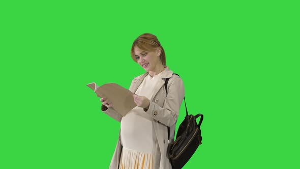 The Pregnant Woman Standing with a Book on a Green Screen, Chroma Key. alt