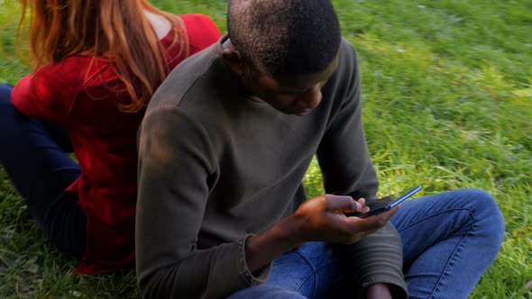 Youth,technology,devices.Mixed lfriends using smartphones sitting on the grass alt