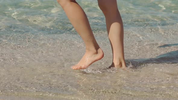 Slim Female Legs and Feet Walking Along Sea Water Waves on Sandy Beach alt