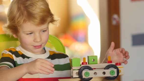 Young blonde boy examines his finished constructed toy vehicle.
