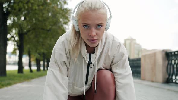 Serious Young Blonde Wearing Headphones Getting Ready for Marathon Then Running alt