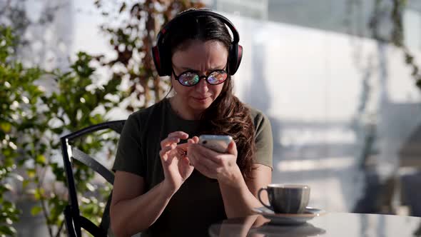 Adult Lady with Crazy Eyeglasses is Using Smartphone Listening to Sound By Wireless Headphones alt