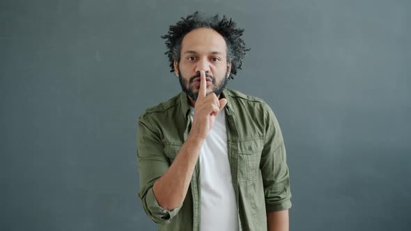 Slow Motion Portrait of Handsome Arab Guy Showing Hush Hand Gesture Looking at Camera alt