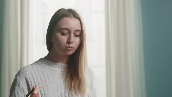 Blonde Girl in White Jacket Holding Chopsticks for Sushi and Straightens Hair alt