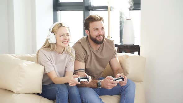 Cheerful Man and Woman Sitting on Sofa in Living Room Playing Computer Video Game