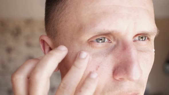 White Metrosexual Man Applying Lotion for Antiaging Treatment Around Eye