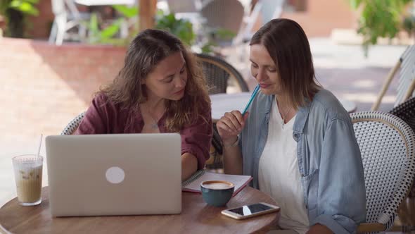 Happy Female Friends Working Together with Laptop at Outdoor Cafe alt