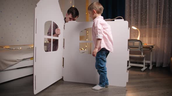 Young Father with Little Son Assembling Toy Cardboard House in Children Bedroom alt
