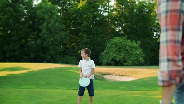 Man, Boy and Woman Playing Frisbee in Park. Family Throwing Frisbee Disc alt