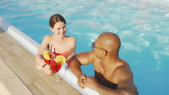 Happy Multiethnic Couple Clinking Glasses in the Swimming Pool