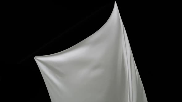 White fabric flowing on black background, Slow Motion alt