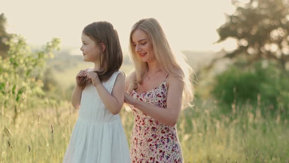 Young Charming Blonde Mother Helps Her Cute Daughter to Dress in a White Dress