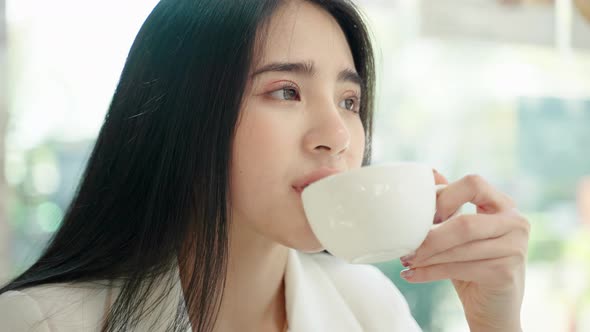 beautiful Asian woman is sitting comfortably sipping coffee in a cafe.