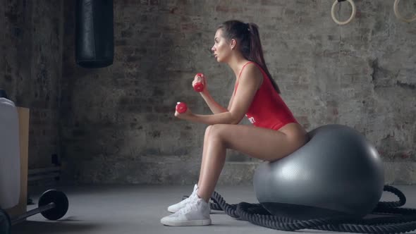 Woman sitting on fitness ball and doing exercises with dumbbells
