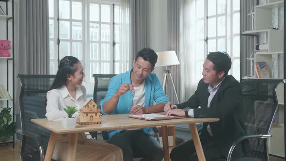 Asian Couple With A House Purchase Contract Paper Receives The Keys From A Real Estate Agent alt