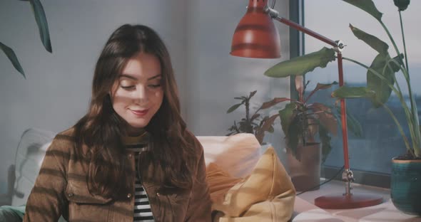 Woman looks out of window whie working on laptop alt