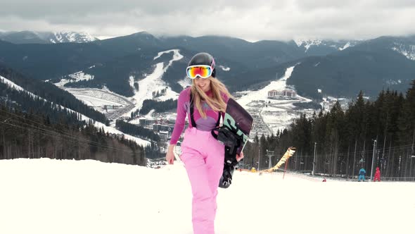 Young Girl Snowboarder is Smiling on the Top of the Mountain alt