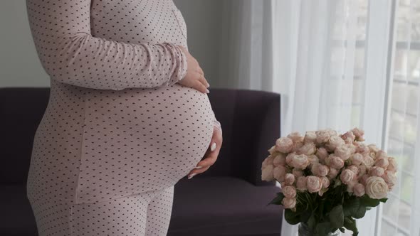 Unrecognisable Pregnant Woman Stroking Her Big Belly Near the Bouquet of Rose Flowers