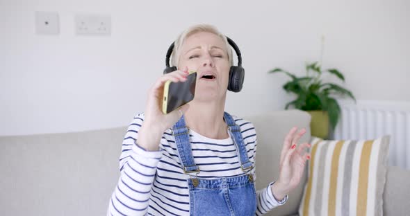 Woman sitting on couch singing and dancing to music from headphones