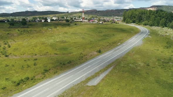 Aerial Countryside Road Running Through Green Fields Towards the Village alt