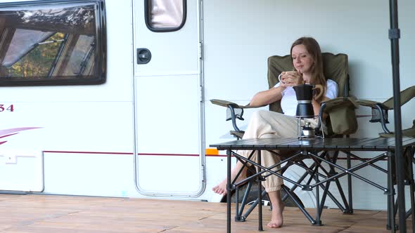 Woman Sitting on Folding Chair Enjoy Evening on Camp Site Next to Camper RV alt
