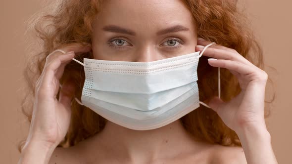Woman Putting On Protective Face Mask Posing Over Beige Background alt