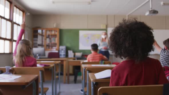 Group of kids wearing face mask raising their hands in the class at school alt