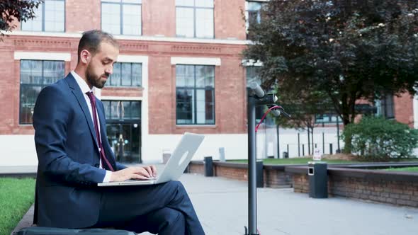 Businessman Outdoor Typing on the Laptop Sitting in a Business District alt