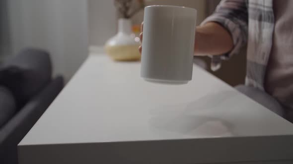 Female Hand Putting White Mug with Drink on Kitchen Counter Indoors alt