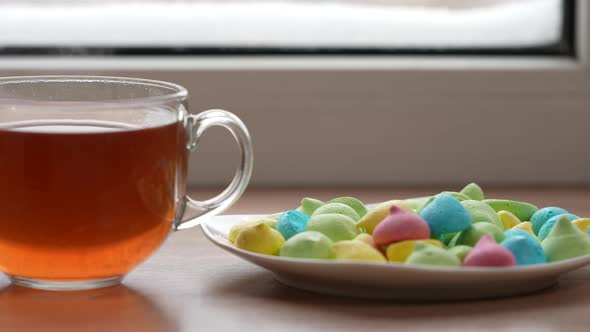 A Large Mug of Tea and Colorful Sweets in a Plate on the Windowsill By the Window in Winter