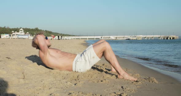 An athletic man does crunches on the beach alt