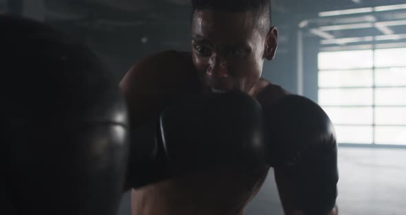 African american man wearing boxing gloves training in empty building punching punchbag alt