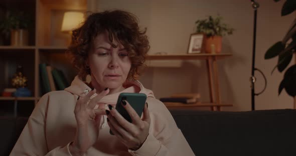 Crop View of Excited Woman with Short Curly Hair Scrolling Phone Screen While Sitting on Sofa at alt