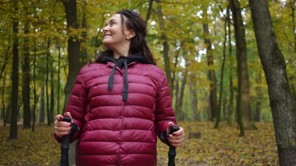 Panning Shot of Happy Mature Caucasian Woman Smiling Admiring Beauty of Autumn Nature in Forest alt