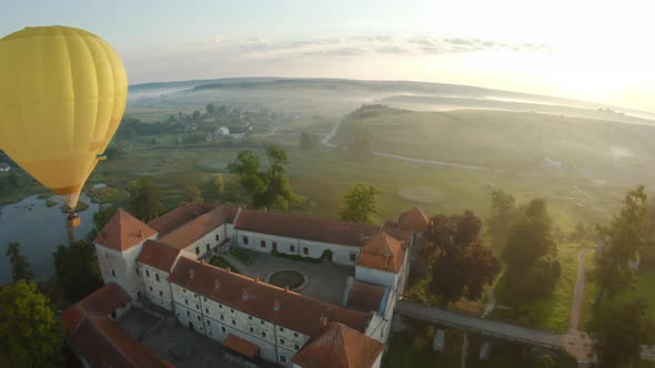 Colorful Hot Air Balloons Fly Over the Medieval Castle and Lake in the Morning Fog. Maneuverable alt