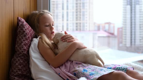 Little Girl Petting Labrador Puppy on Windowsill alt