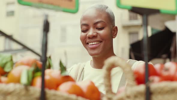 Smiling woman shopping fresh tomatoes at a market stand alt