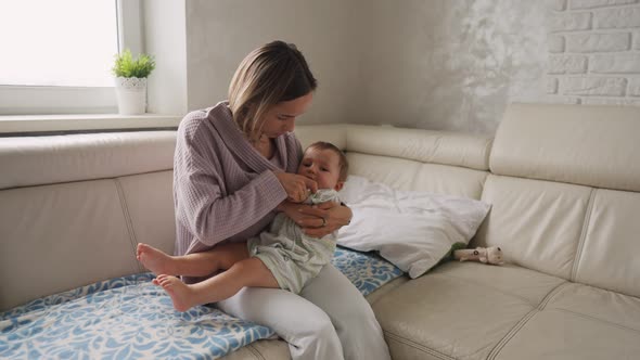 Worried Young Mother Sitting on Sofa Beside Her Sick Son with High Fever