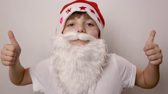Girl with Artificial Beard in Santa Claus Hat Raises Thumbs Up on White Backdrop