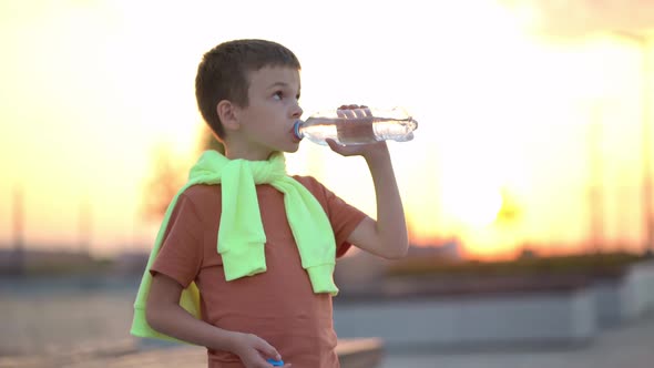 Young Man Drinking Water From a Plastic Bottle in the City at Sunset