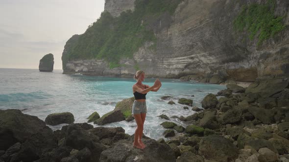 Selfie taking woman on shore of tropical island with grand cliffs, Nusa Penida alt