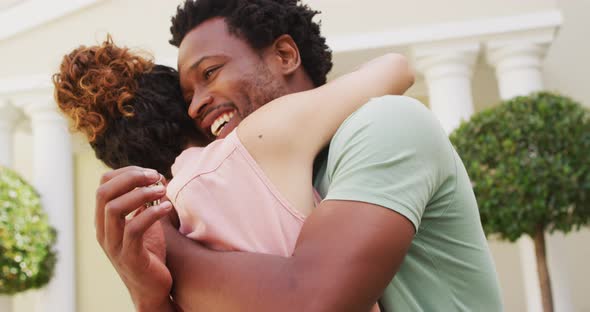 Happy biracial couple embracing with joy in front of new house alt