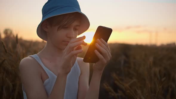 Boy Uses the Phone in the Golden Wheat Field at Sunset