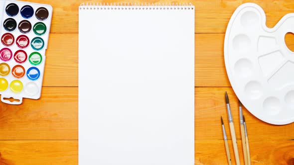 The school teacher lays out on the table a palette, a sketchbook, bright colorful multi-colored