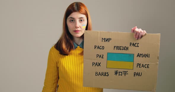 Sad Girl Hold a Placard with Ukraine Flag and Peace Text in Alla Languages alt