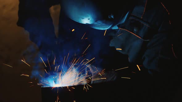 A Welder in a Protective Helmet and Clothes Welds Metal Sparks Illuminate It alt