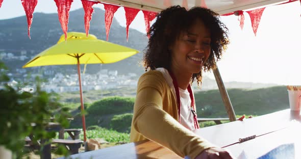 African american woman wearing apron smiling while cleaning the food truck alt