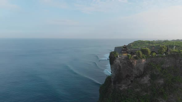 Aerial orbit shot around a Temple located near high rough cliffs and surrounded with ocean in Bali alt