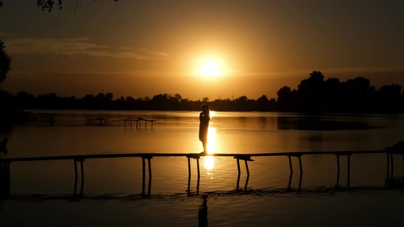 A little girl on a wooden pier on the lake throws her hair back. Silhouette at sunset.